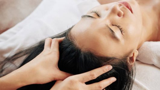 Close-up image of beautician massaging head of female client relaxing on massage bed